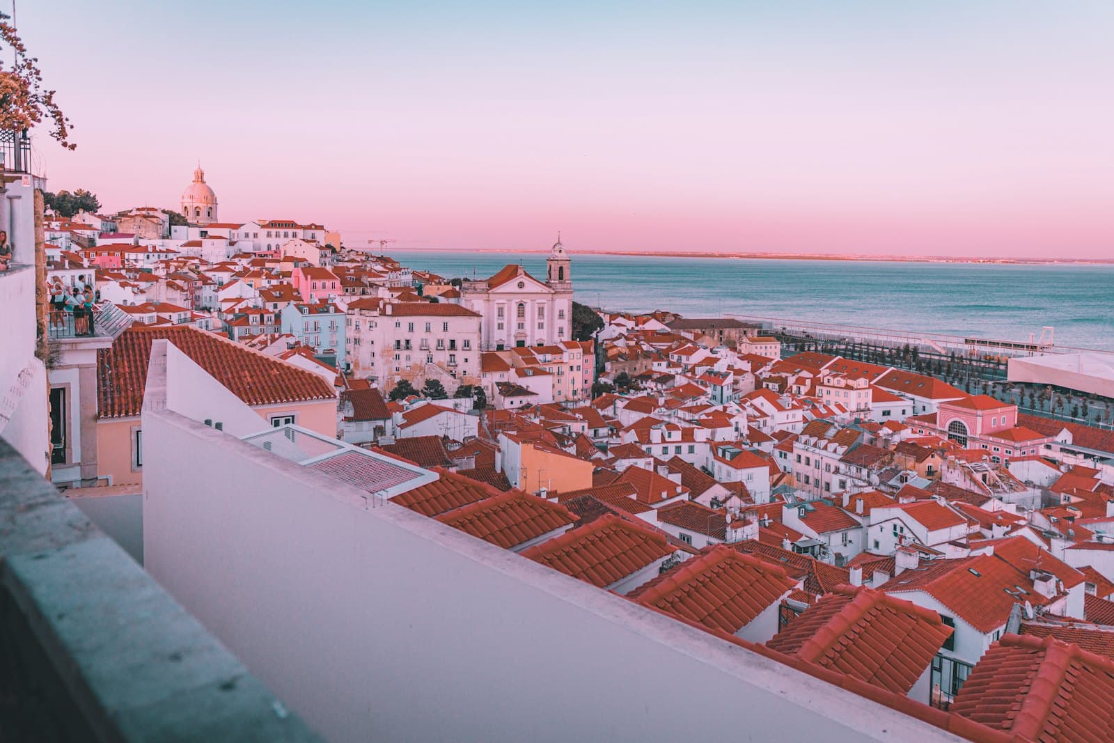 Terracotta rooftops stepping down to the river at dusk in Lisbon